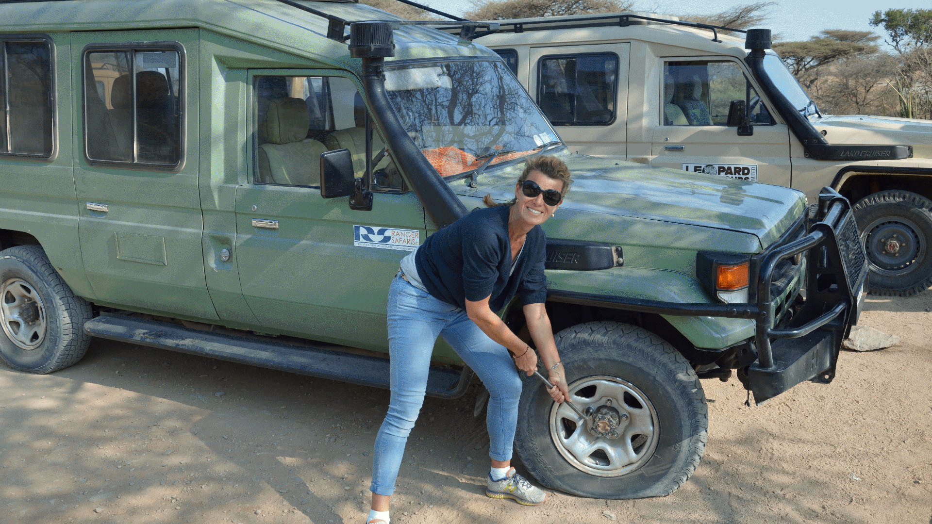 Petra Kirsch wechselt lachend einen Reifen an einem Safari-Geländewagen