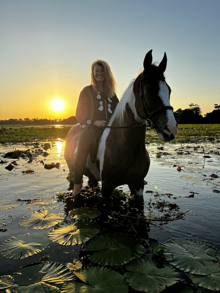 Petra Kirsch auf einem gescheckten Pferd im Wasser zwischen Seerosen bei Sonnenuntergang